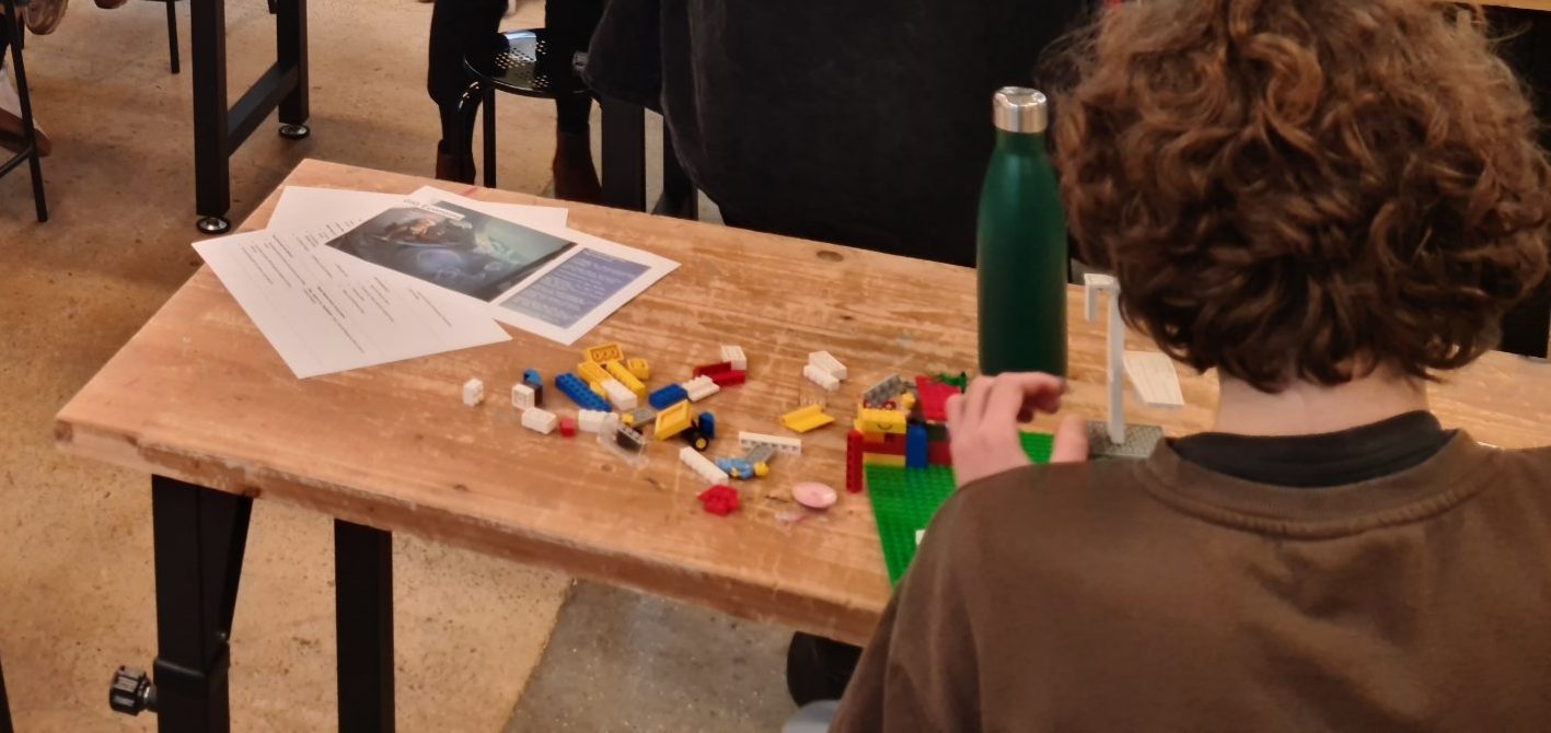 Ein Kind baut an seinem Lego-Betrieb, daneben liegen Auftrag und Material.